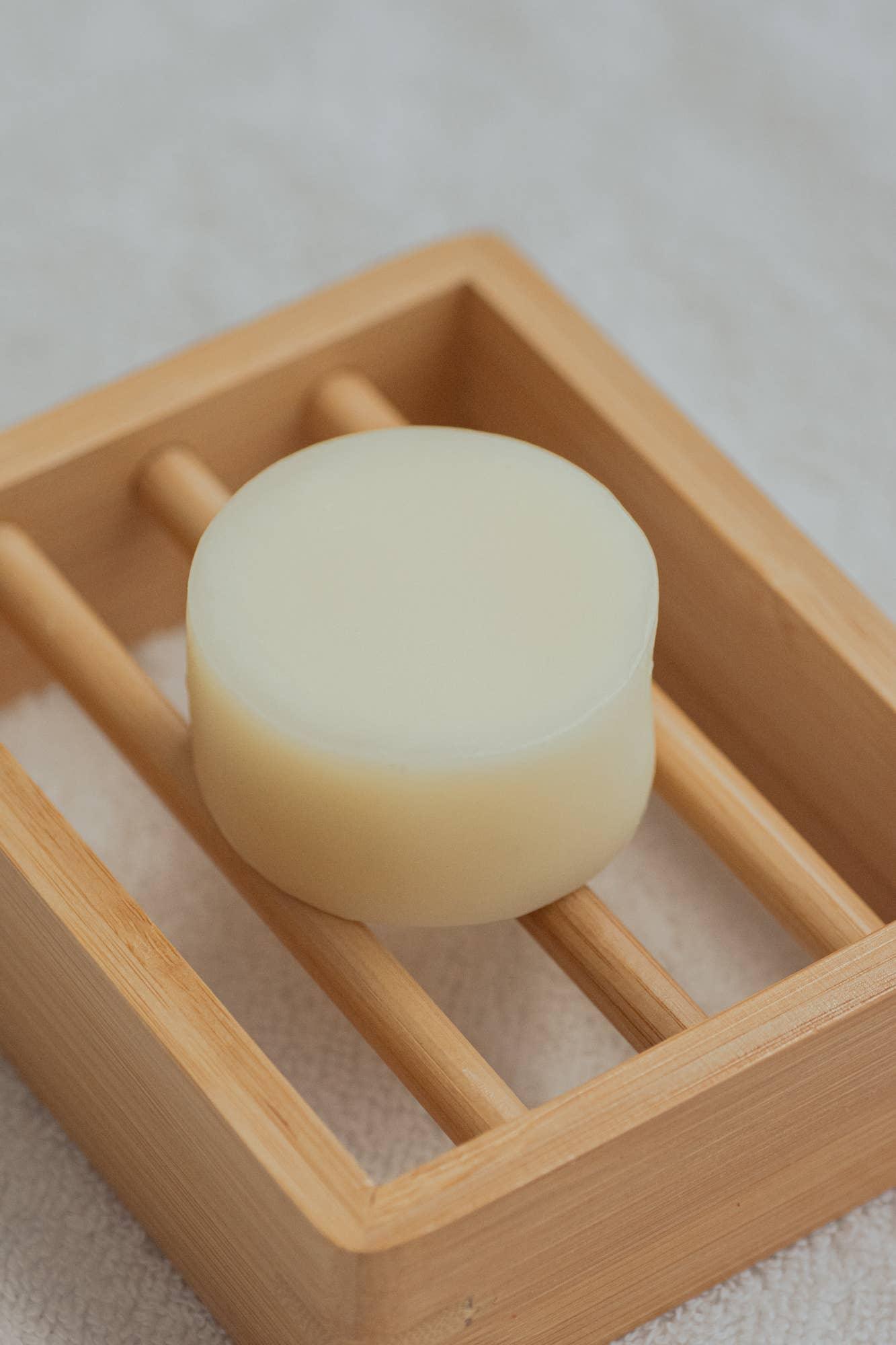 Round natural soap on bamboo soap dish with white towel background. Come see us at Awaken, Franklin, Tennessee