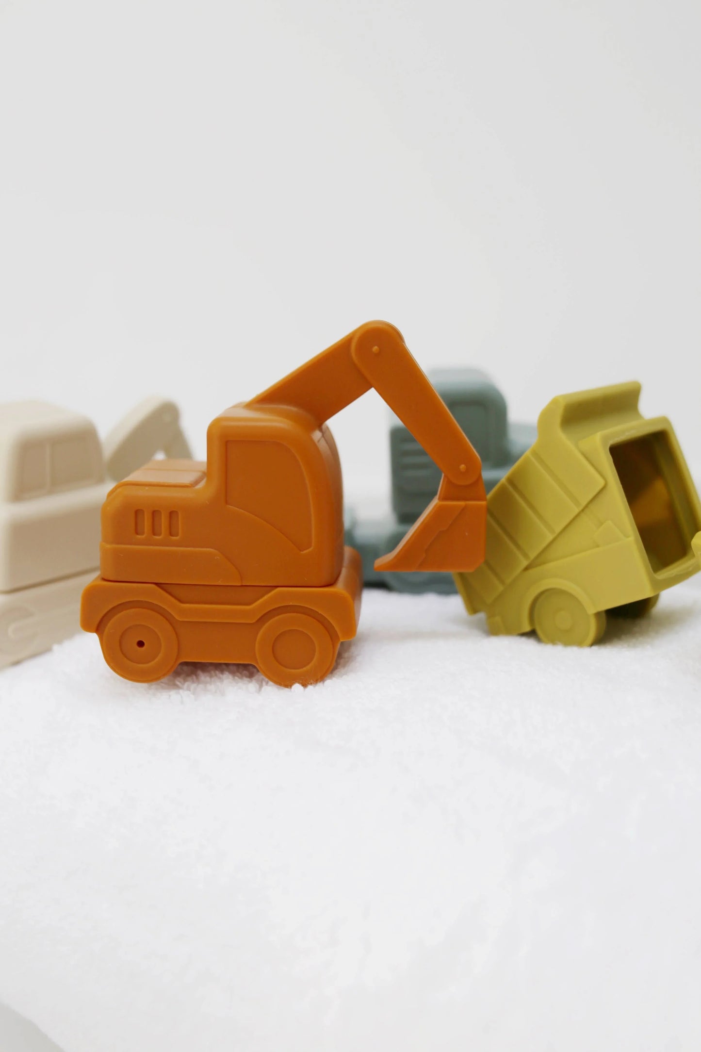 Plastic toy construction vehicles in muted colors on white fabric surface. Come see us at Awaken, Franklin, Tennessee