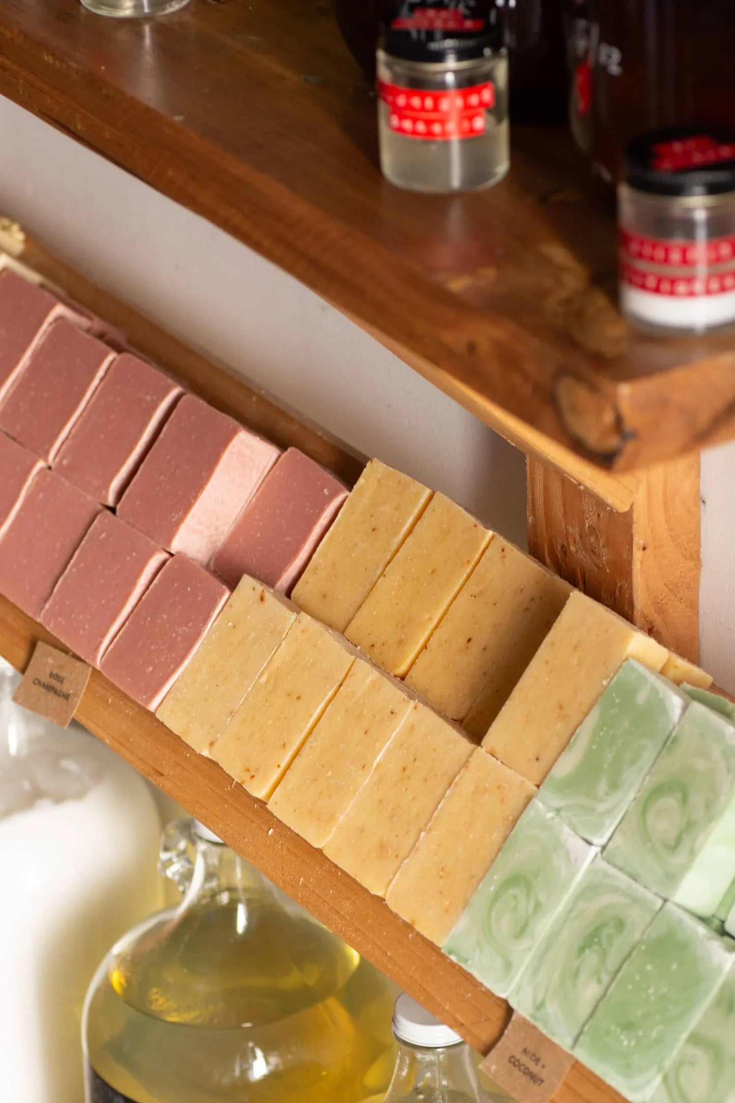 Handmade soap bars in pink, yellow, and green on wooden shelf with essential oils below. Come see us at Awaken, Franklin, Tennessee