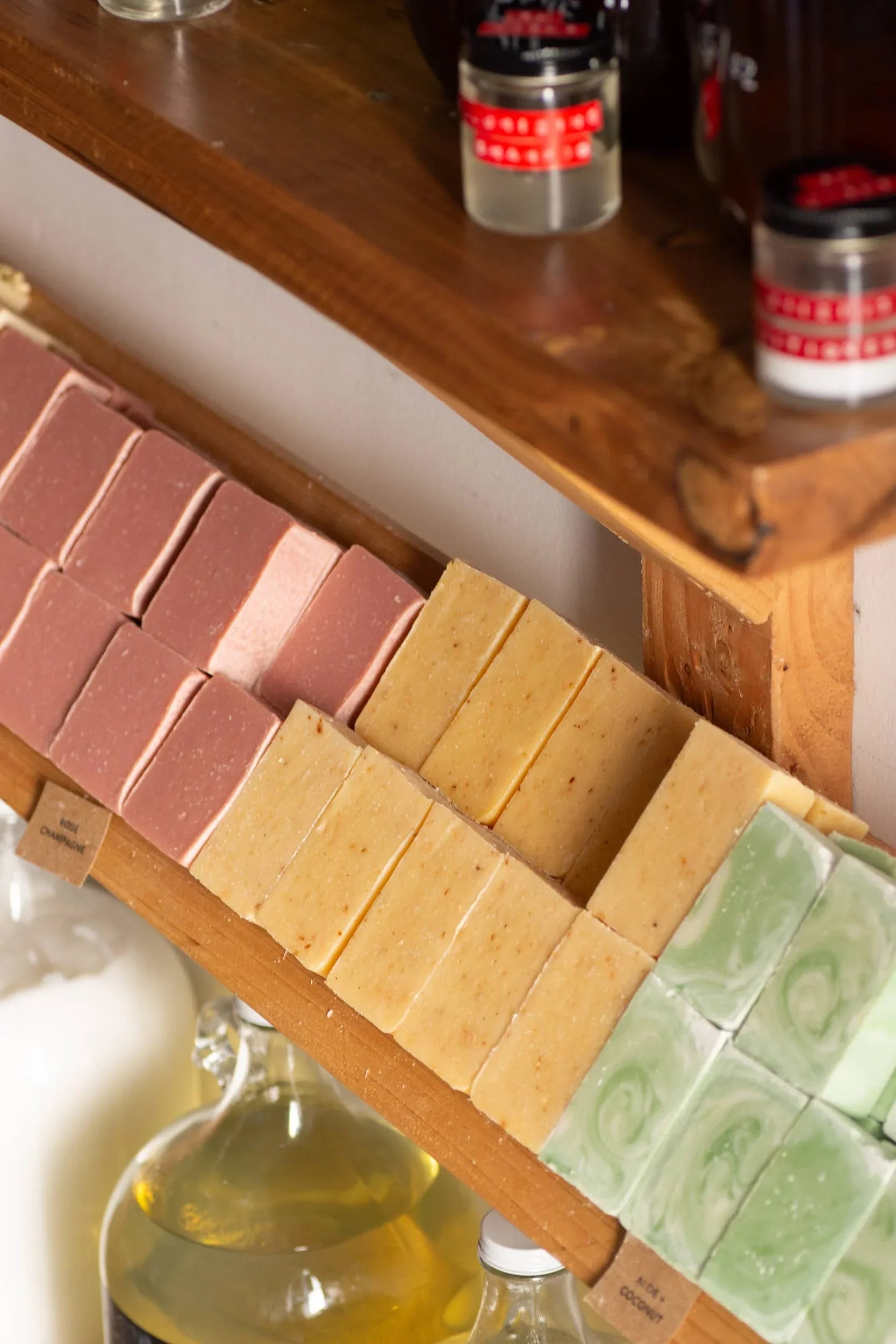 Handmade soap bars in pink, yellow, and green on wooden shelf with essential oils below. Come see us at Awaken, Franklin, Tennessee
