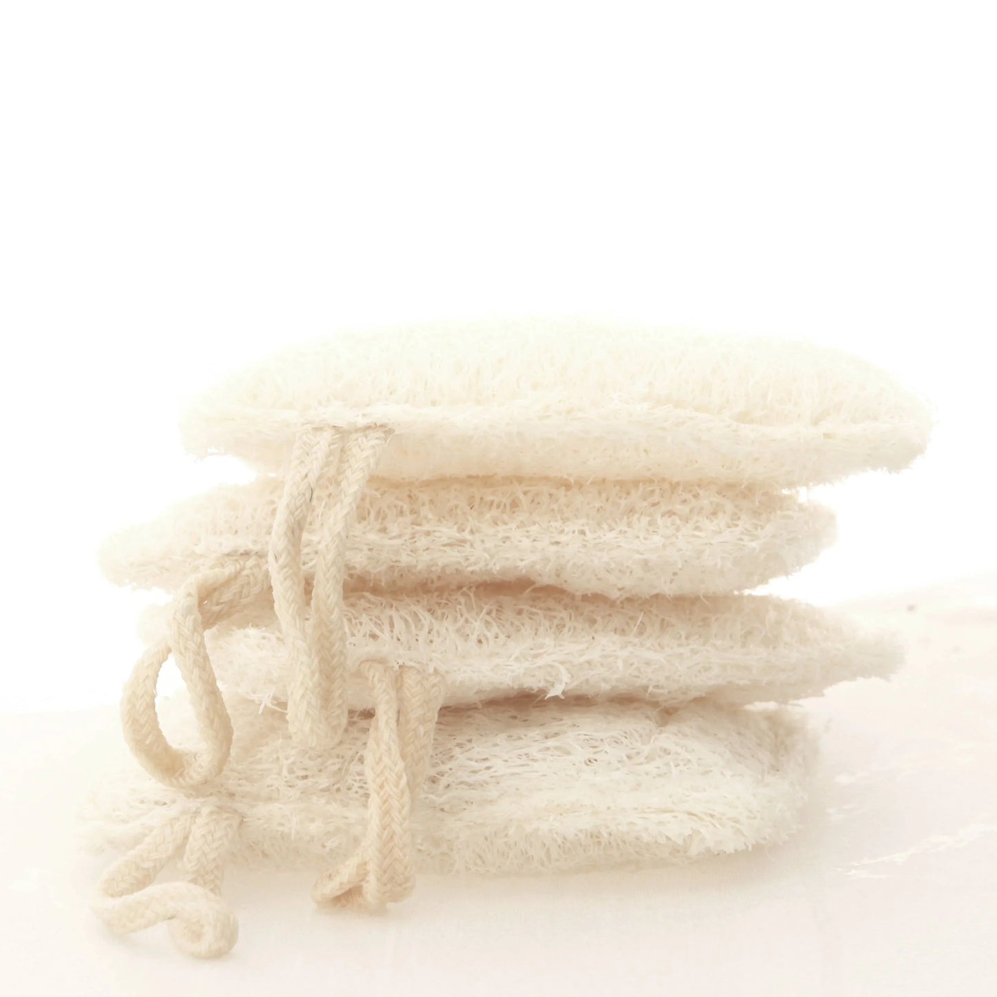 Stack of natural loofah sponges with rope loops on white surface, eco-friendly bath accessories. Come see us at Awaken, Franklin, Tennessee