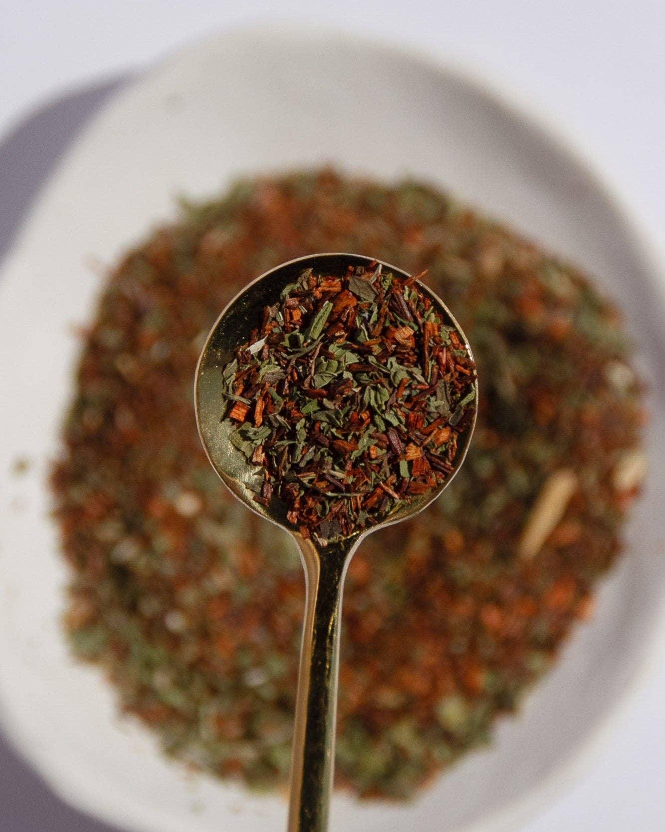 Gold spoon filled with loose herbal tea leaves over a white plate, Come see us at Awaken, Franklin, Tennessee
