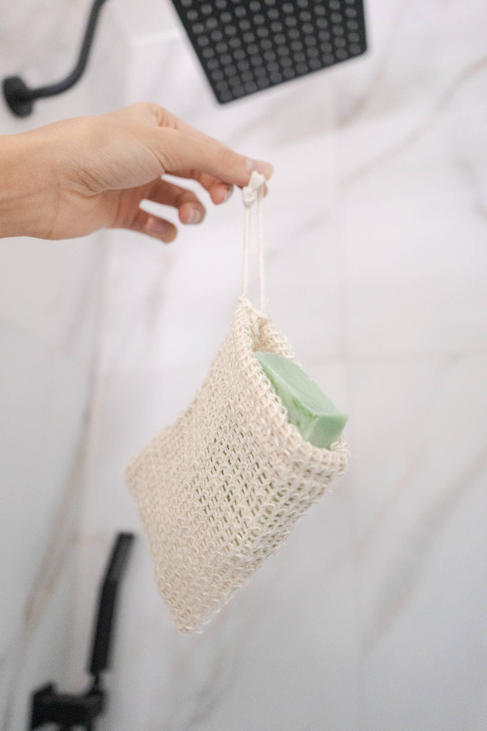Hand holding a woven soap pouch with green soap in a bathroom setting. Come see us at Awaken, Franklin, Tennessee
