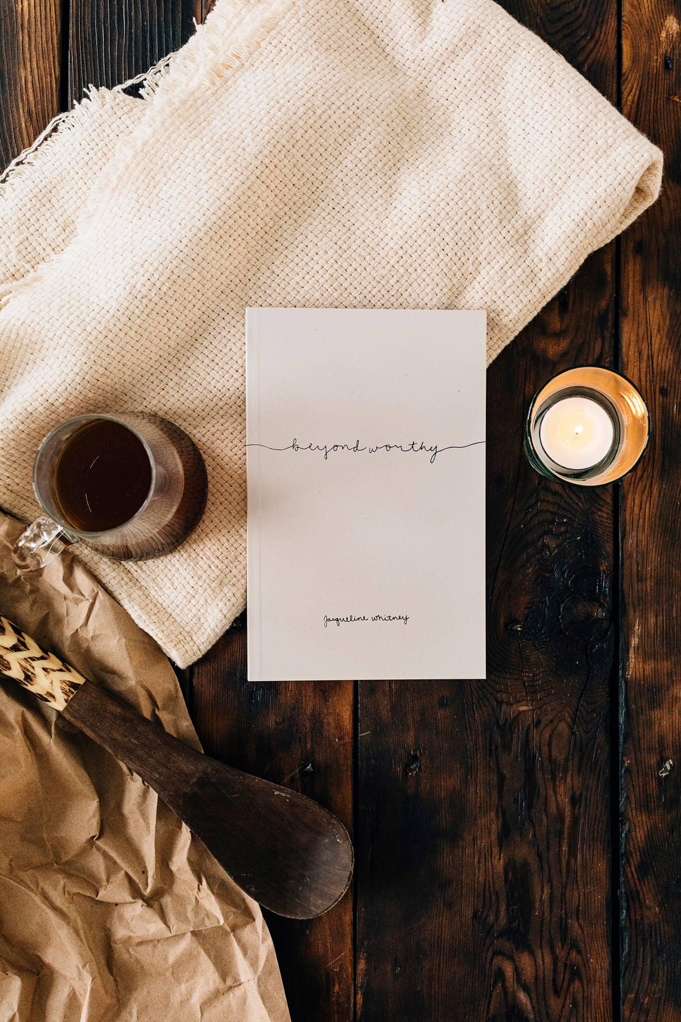 Book titled 'beyond worthy' by Jacqueline Whitney on wooden table with tea, candle, and woven cloth. Come see us at Awaken, Franklin, Tennessee