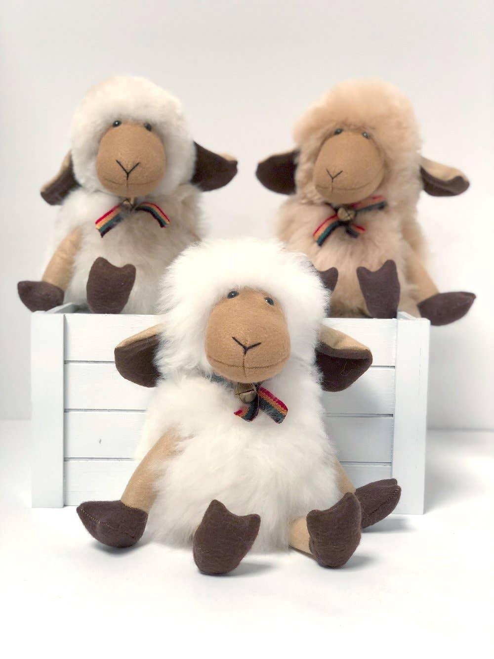 Three fluffy plush sheep toys with brown faces and rainbow bow ties on a white crate. Come see us at Awaken, Franklin, Tennessee