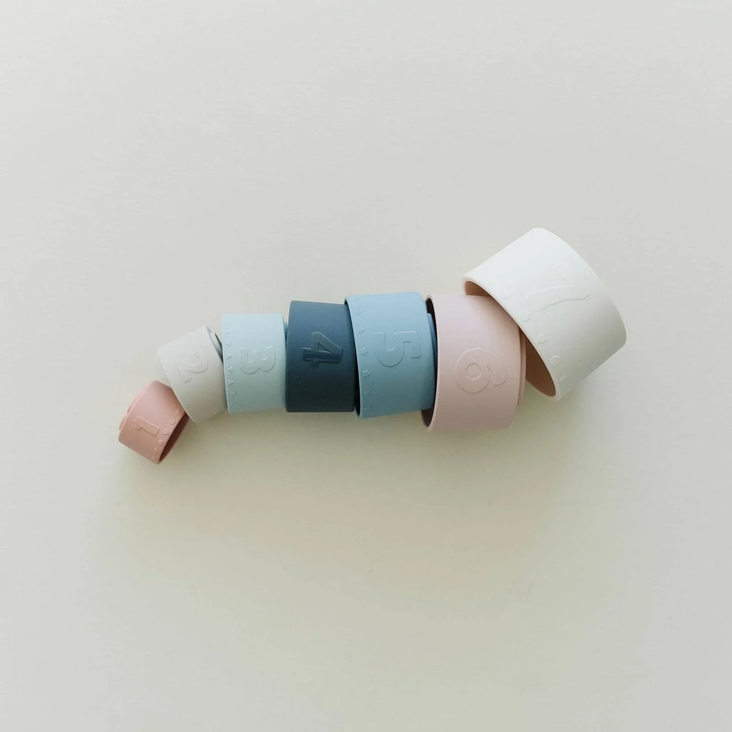 Stacked pastel silicone rings numbered 1 to 7 on white background, minimalist design. Come see us at Awaken, Franklin, Tennessee