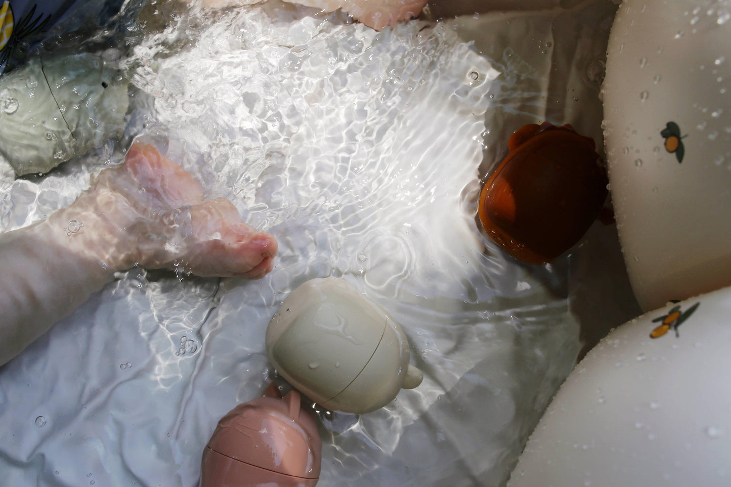 Baby's feet splashing in water with floating soft animal toys and inflatable with fruit print. Come see us at Awaken, Franklin, Tennessee