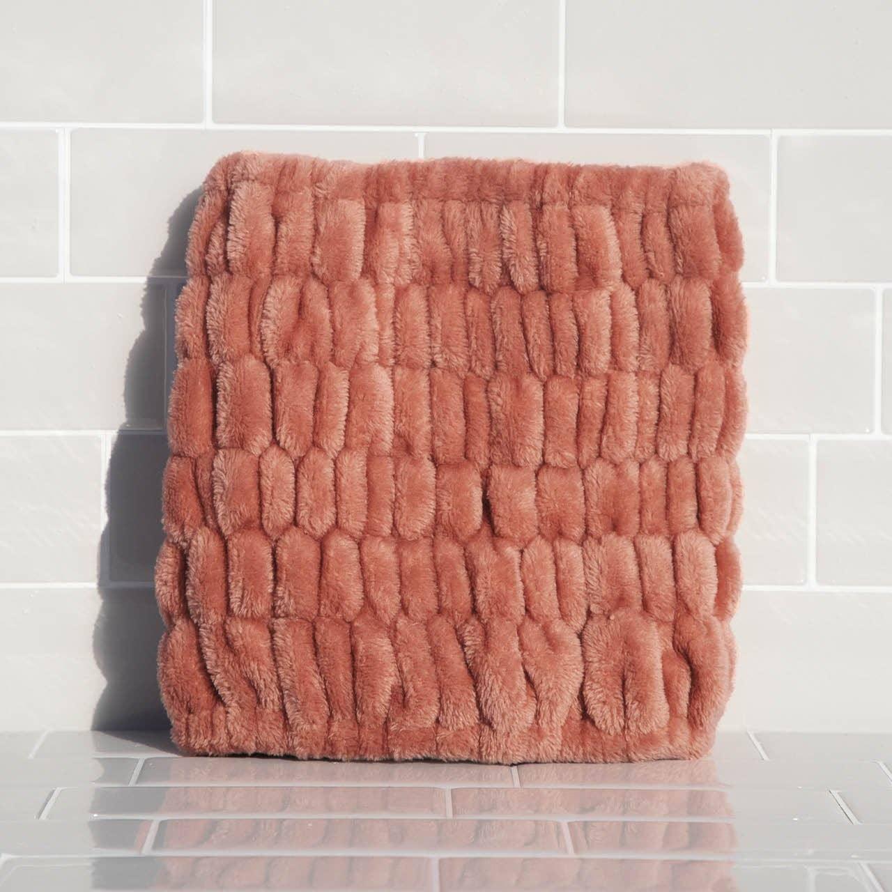 Soft textured plush rose-colored cushion against white tiled wall. Come see us at Awaken, Franklin, Tennessee