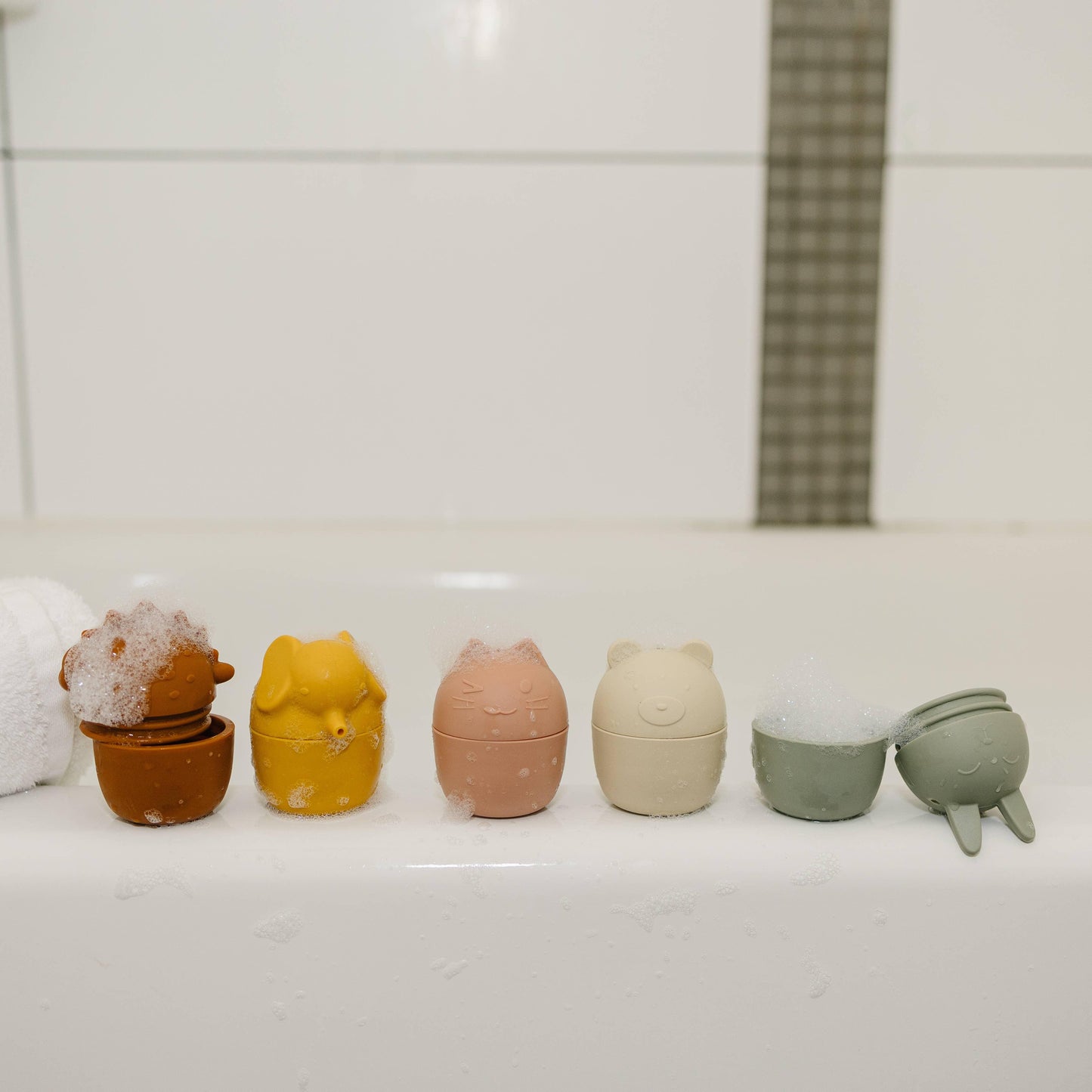 Cute animal-shaped bath toys with bubbles on a white bathtub edge in a tiled bathroom. Come see us at Awaken, Franklin, Tennessee