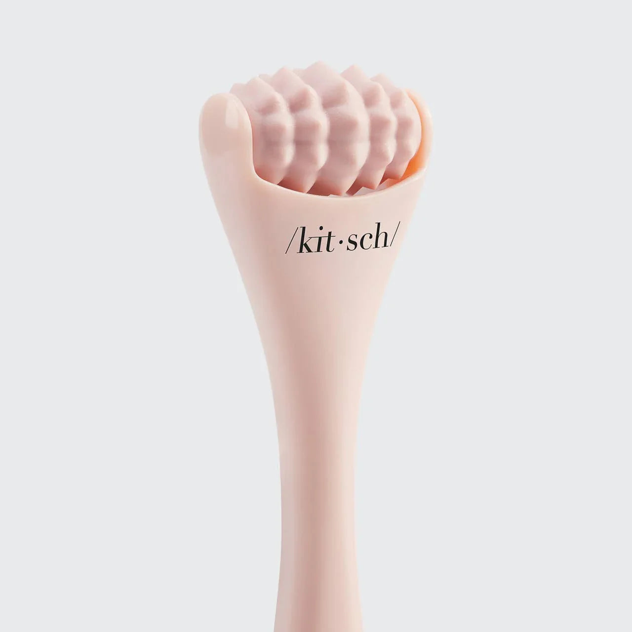 Close-up of pink textured facial roller beauty tool labeled kitsch on white background. Come see us at Awaken, Franklin, Tennessee