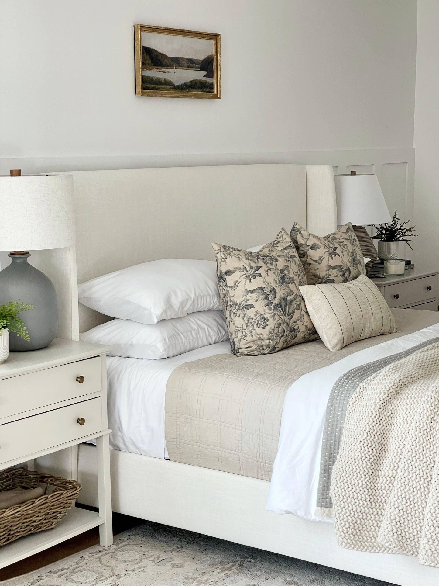 Neutral bedroom with beige upholstered bed, floral pillows, cozy knit blanket, and nightstands. Come see us at Awaken, Franklin, Tennessee