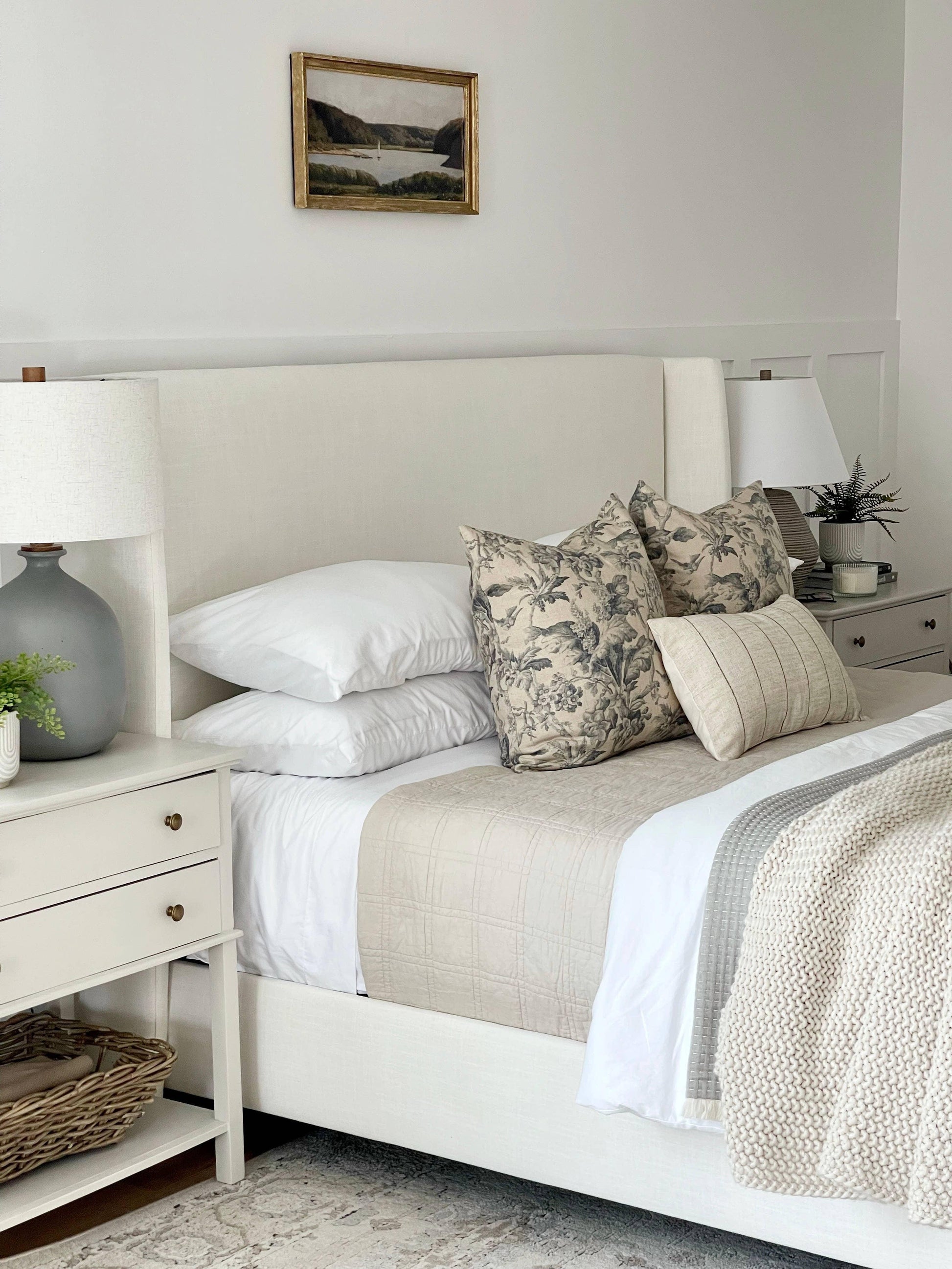 Neutral bedroom with beige upholstered bed, floral pillows, cozy knit blanket, and nightstands. Come see us at Awaken, Franklin, Tennessee