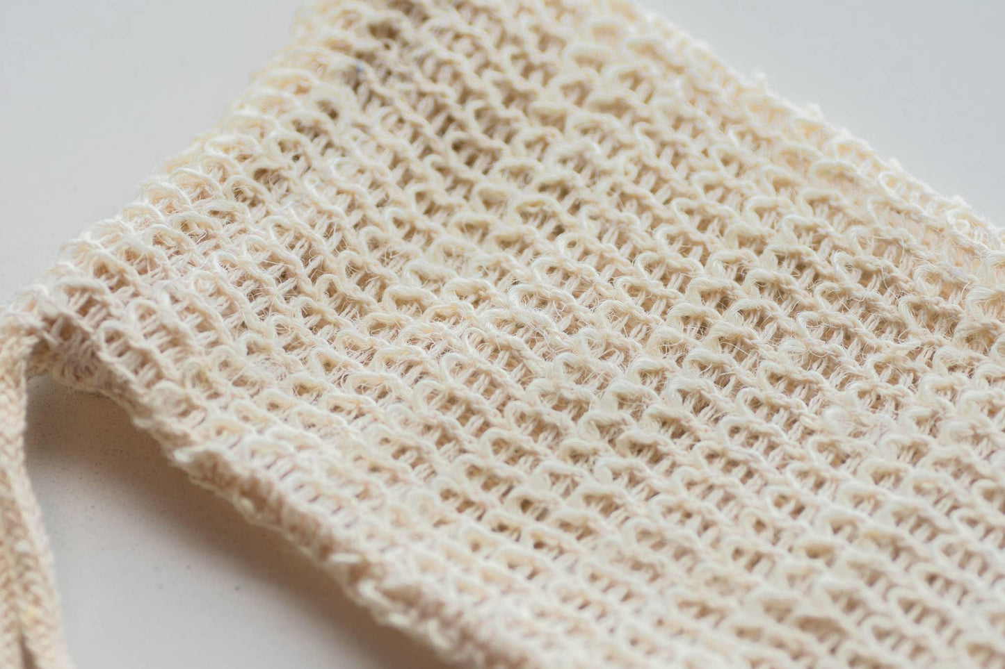 Closeup of woven beige cotton mesh bag on white surface, eco-friendly tote. Come see us at Awaken, Franklin, Tennessee
