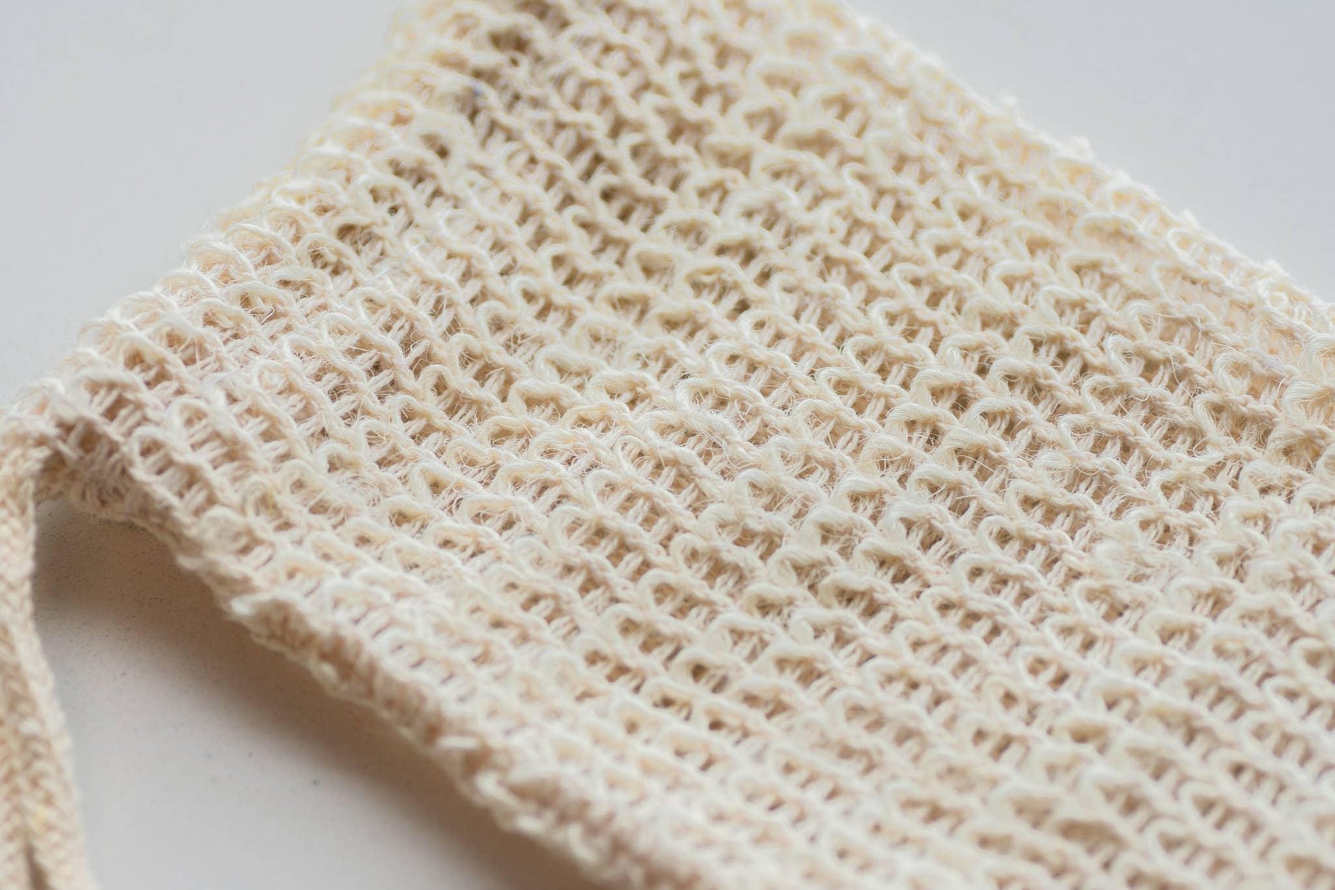 Closeup of woven beige cotton mesh bag on white surface, eco-friendly tote. Come see us at Awaken, Franklin, Tennessee