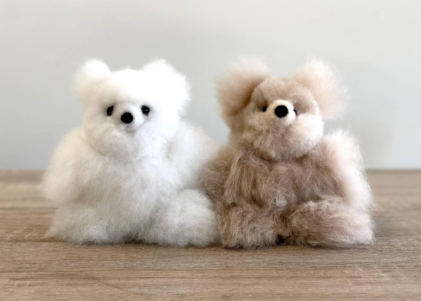 Two fluffy handmade teddy bears in white and beige on a wooden surface. Come see us at Awaken, Franklin, Tennessee