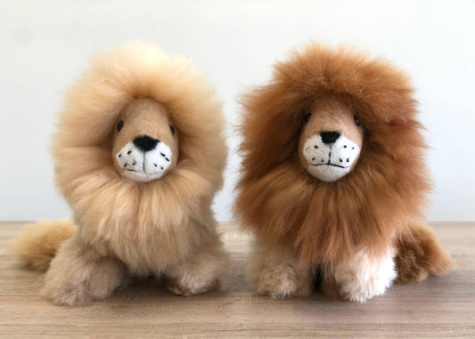 Two plush lion toys with fluffy manes on wooden surface, soft stuffed animals. Come see us at Awaken, Franklin, Tennessee