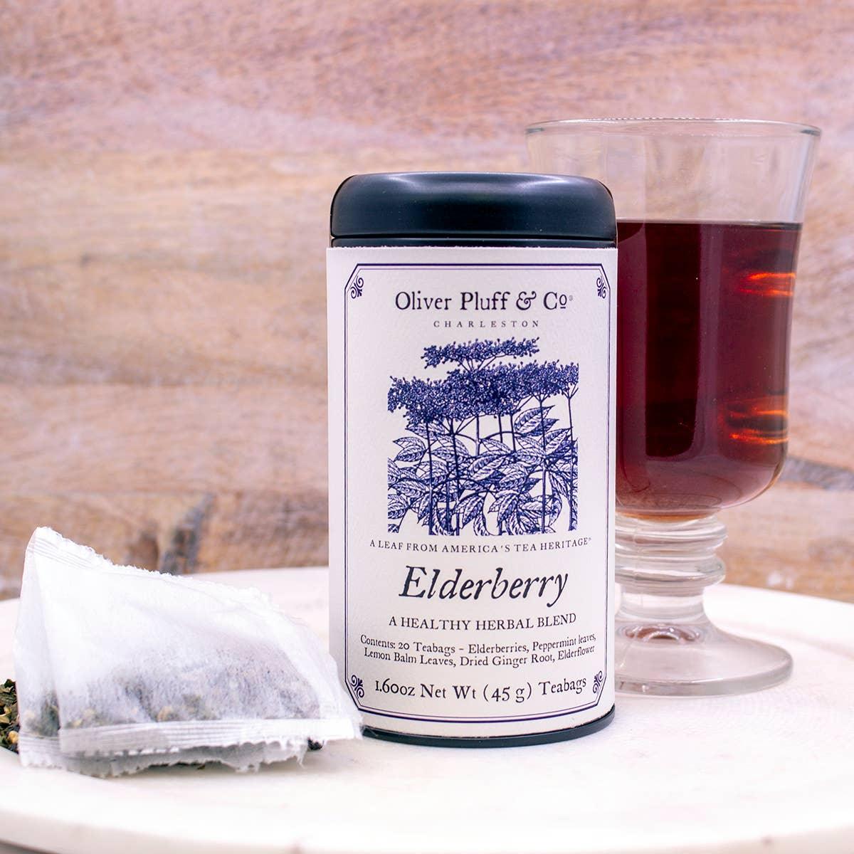 Oliver Pluff Elderberry herbal tea tin, tea bag, and glass of brewed tea on white table. Come see us at Awaken, Franklin, Tennessee