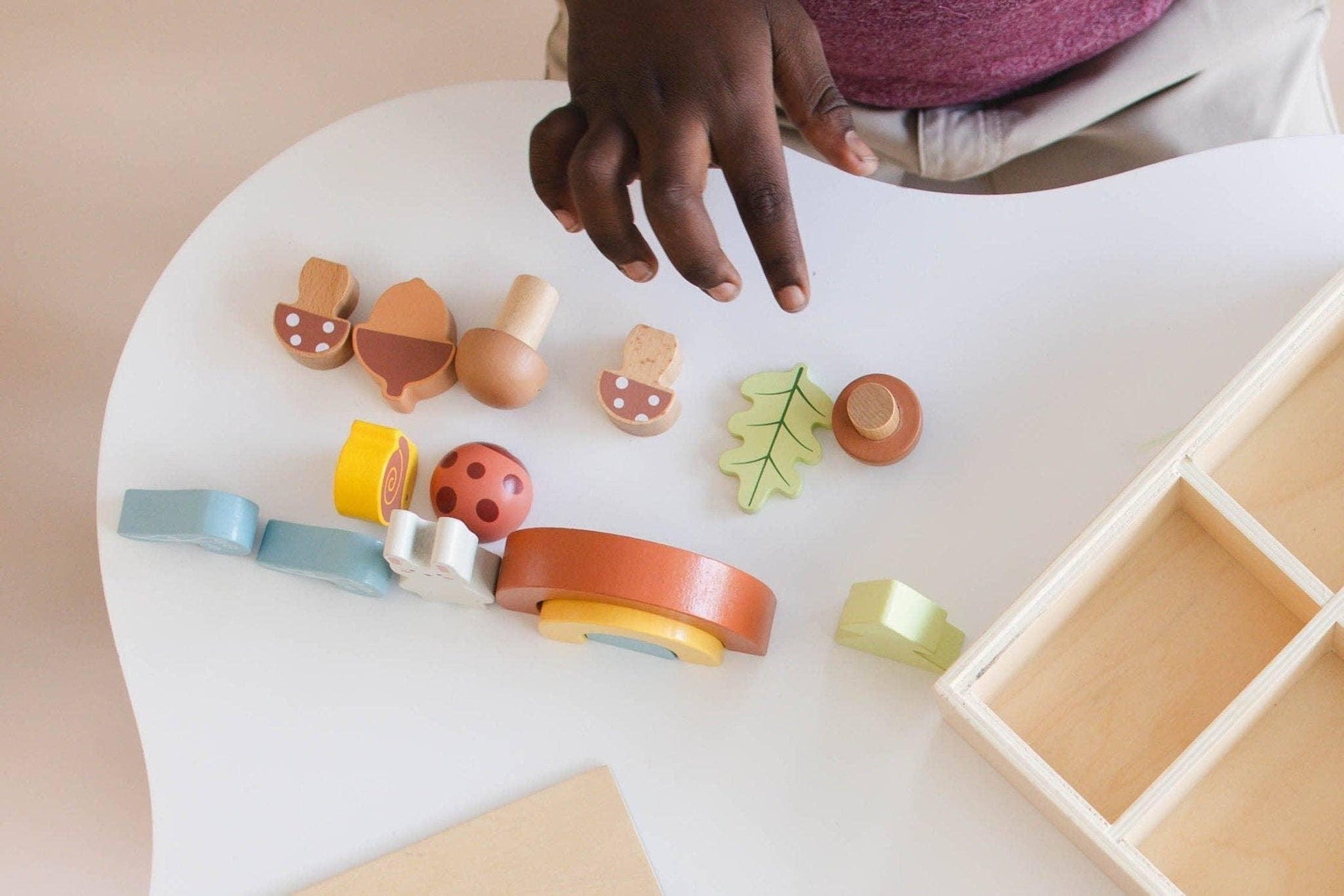 Child's hand arranging colorful wooden toys on white table with wooden organizer nearby. Come see us at Awaken, Franklin, Tennessee