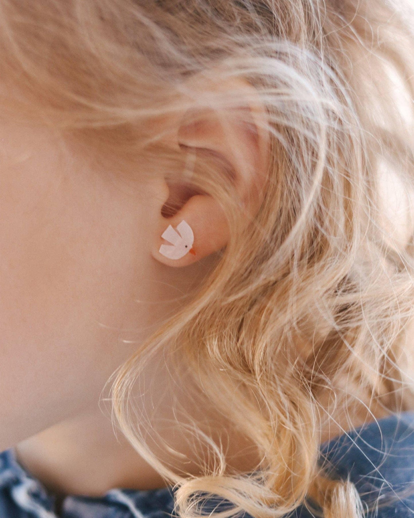 Close-up of child with curly blonde hair wearing white bird-shaped stud earring. Come see us at Awaken, Franklin, Tennessee