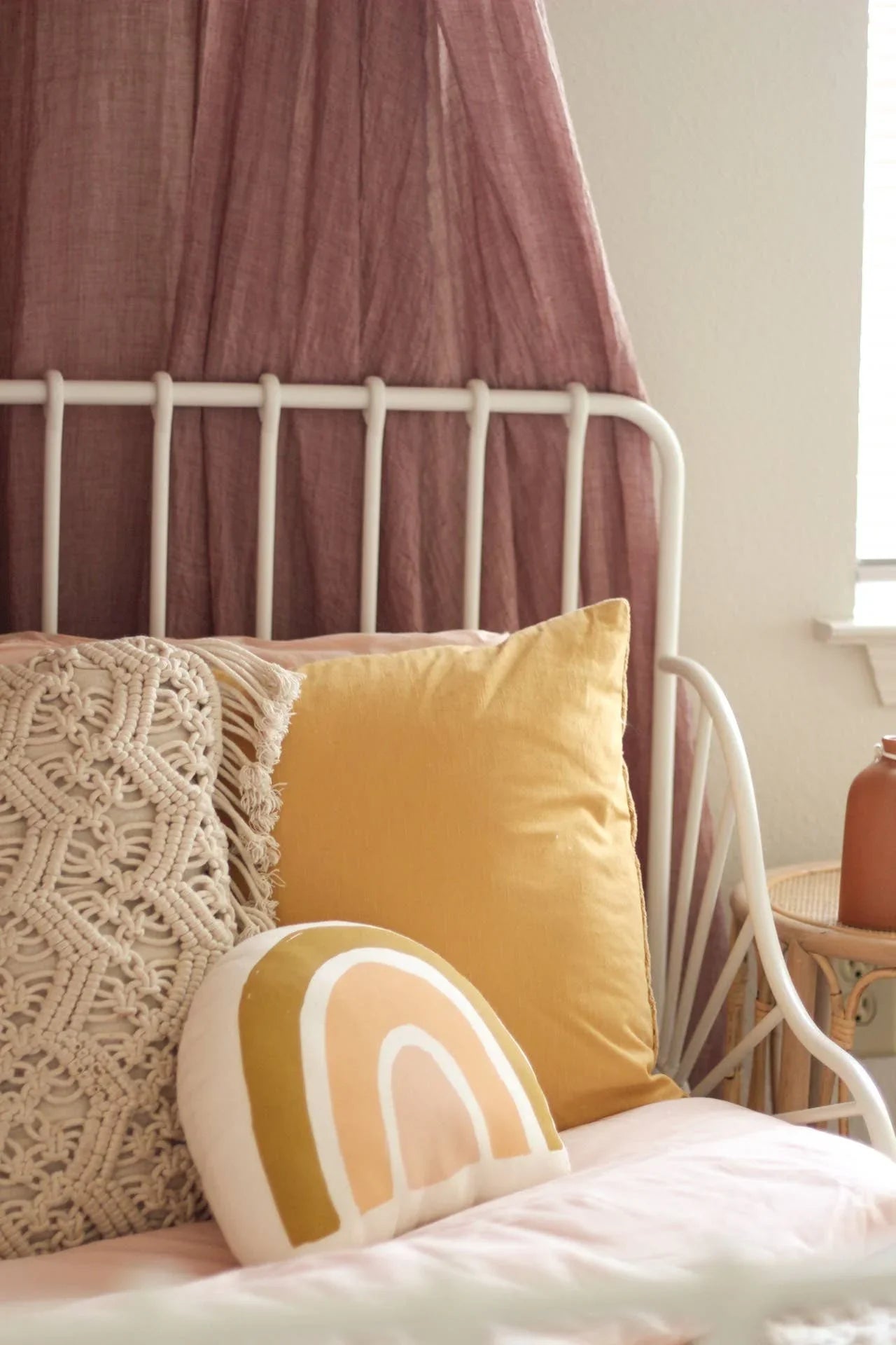 Cozy bed with yellow, macrame, and rainbow pillows, white metal frame, Come see us at Awaken, Franklin, Tennessee