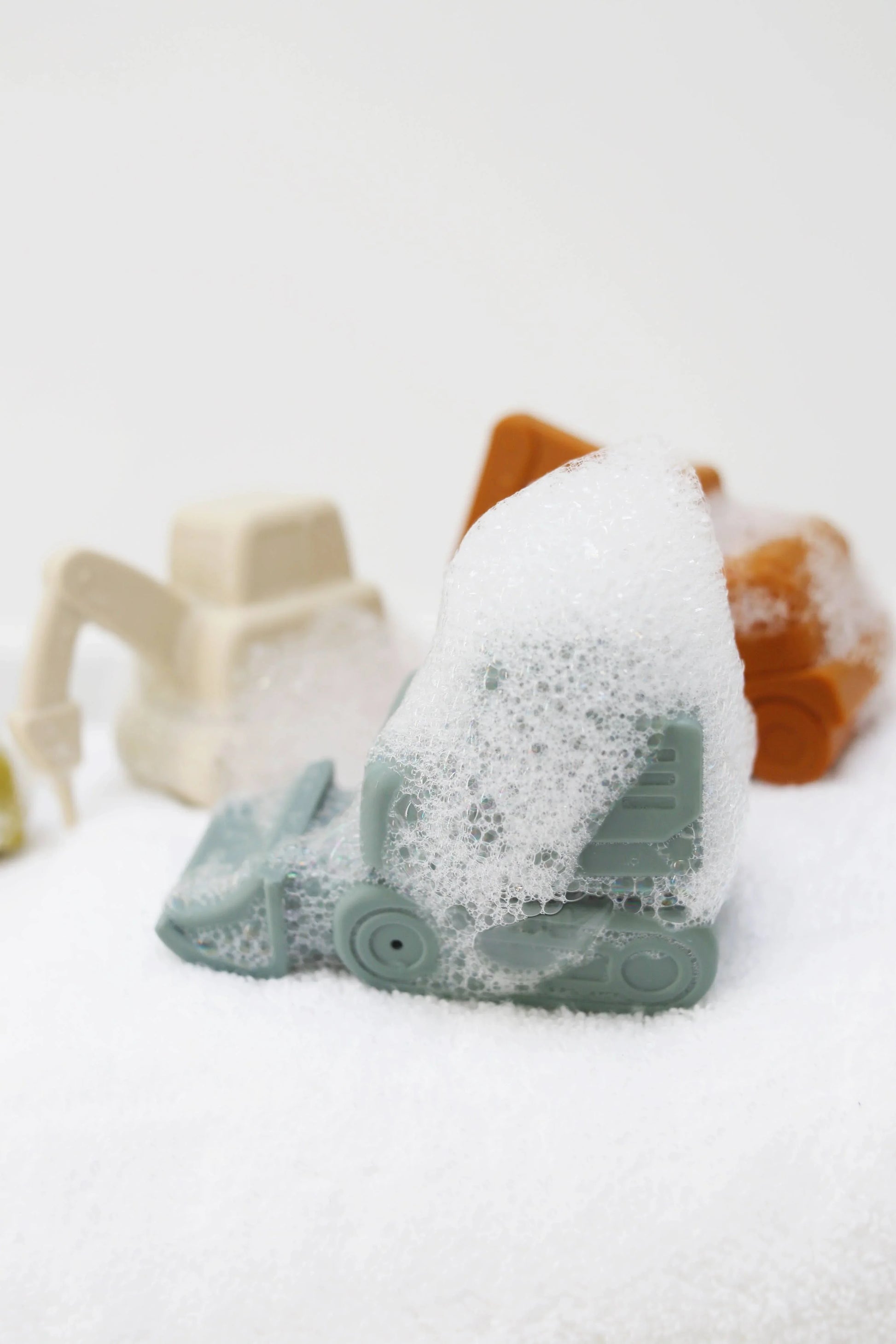 Small toy construction vehicles covered in soap foam on a white towel. Come see us at Awaken, Franklin, Tennessee