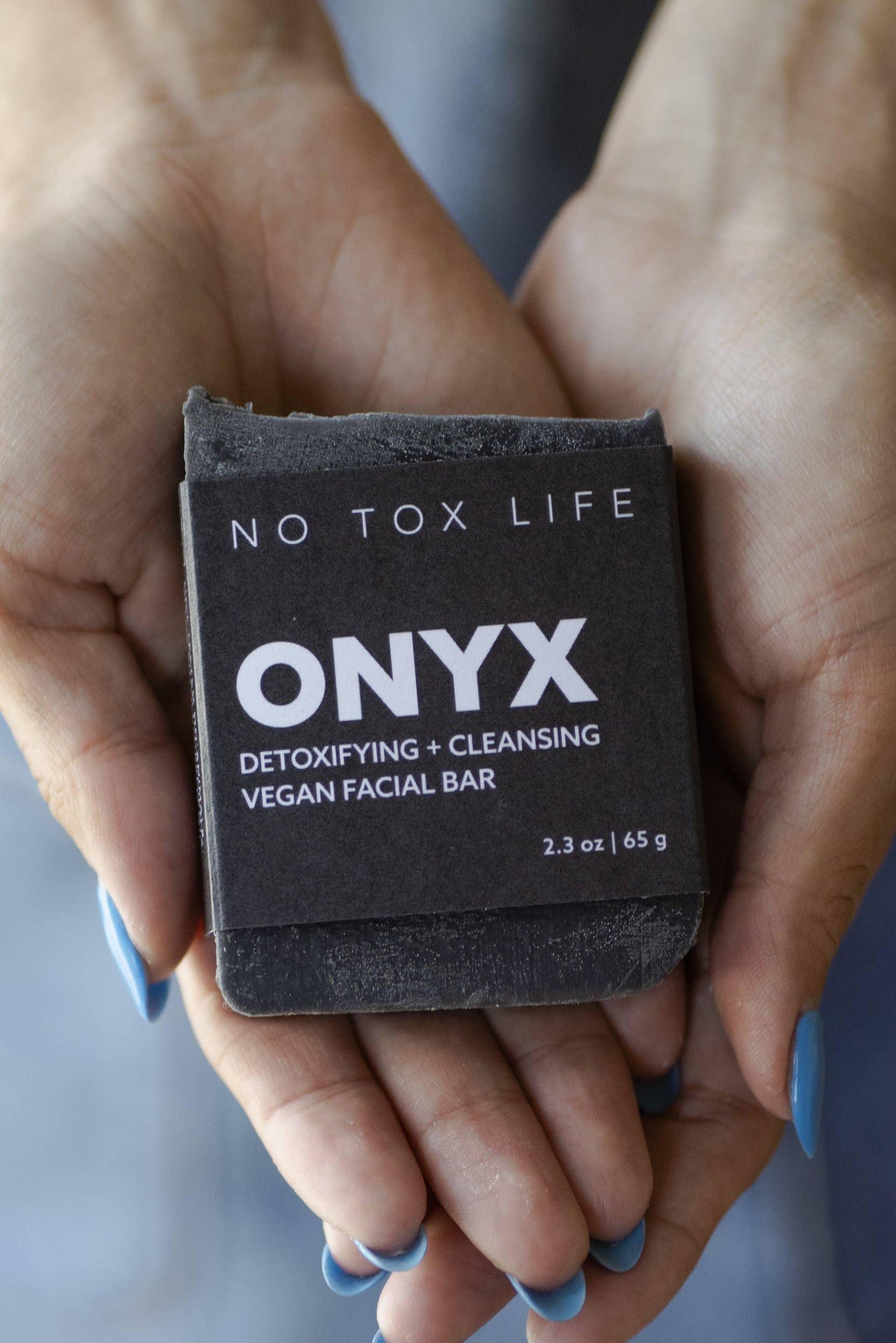 Hands with blue nails holding ONYX detoxifying and cleansing vegan facial bar, Come see us at Awaken, Franklin, Tennessee