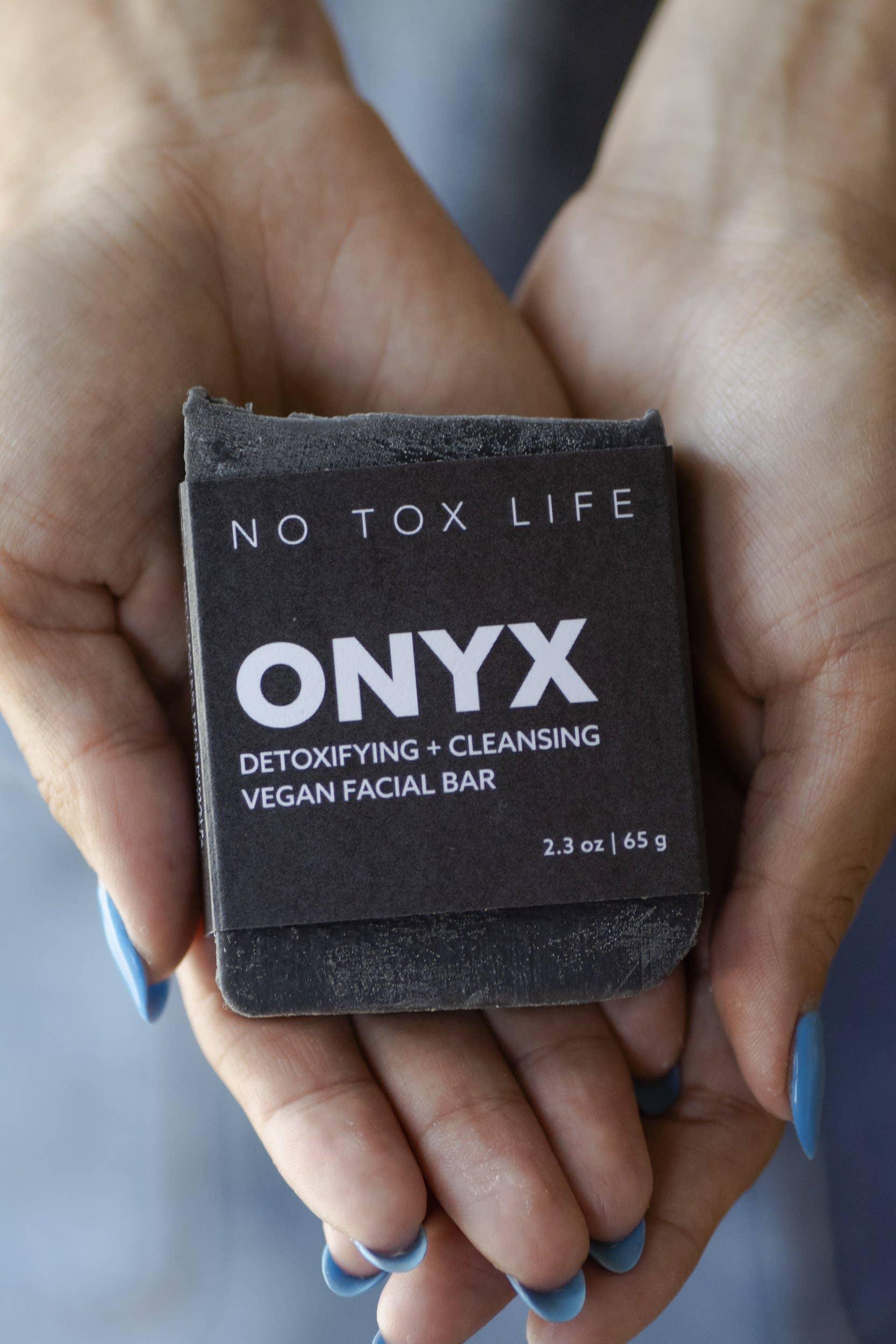 Hands with blue nails holding ONYX detoxifying and cleansing vegan facial bar, Come see us at Awaken, Franklin, Tennessee