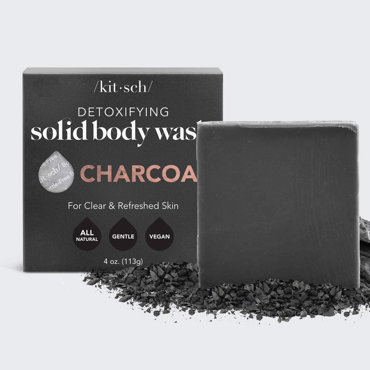 Charcoal detoxifying solid body wash soap bar and black packaging with natural vegan label, on charcoal pieces. Come see us at Awaken, Franklin, Tennessee