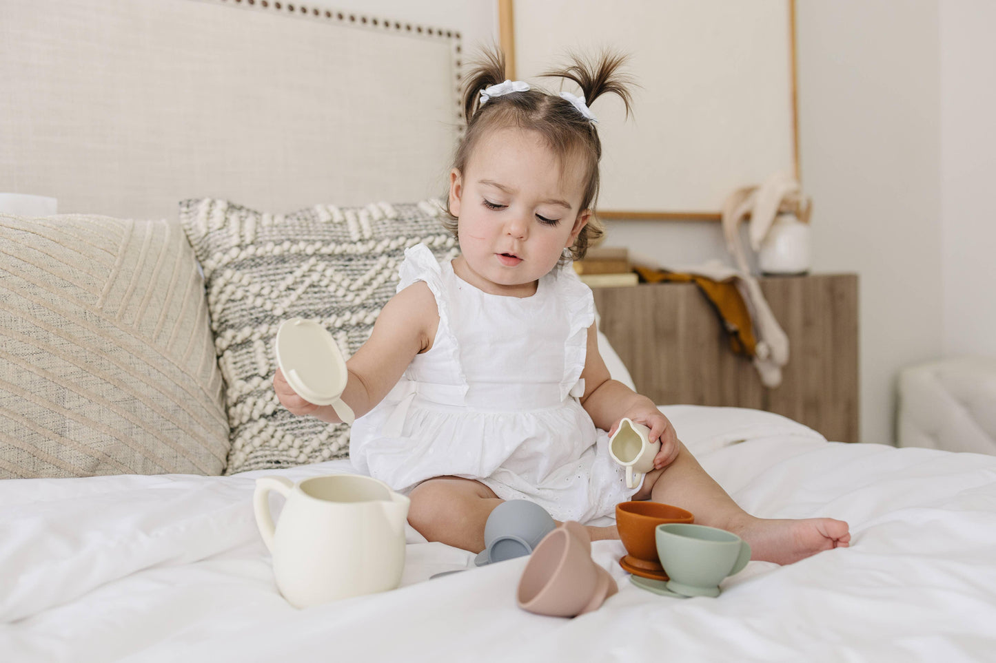 Toddler girl in white dress plays with toy tea set on bed, Come see us at Awaken, Franklin, Tennessee