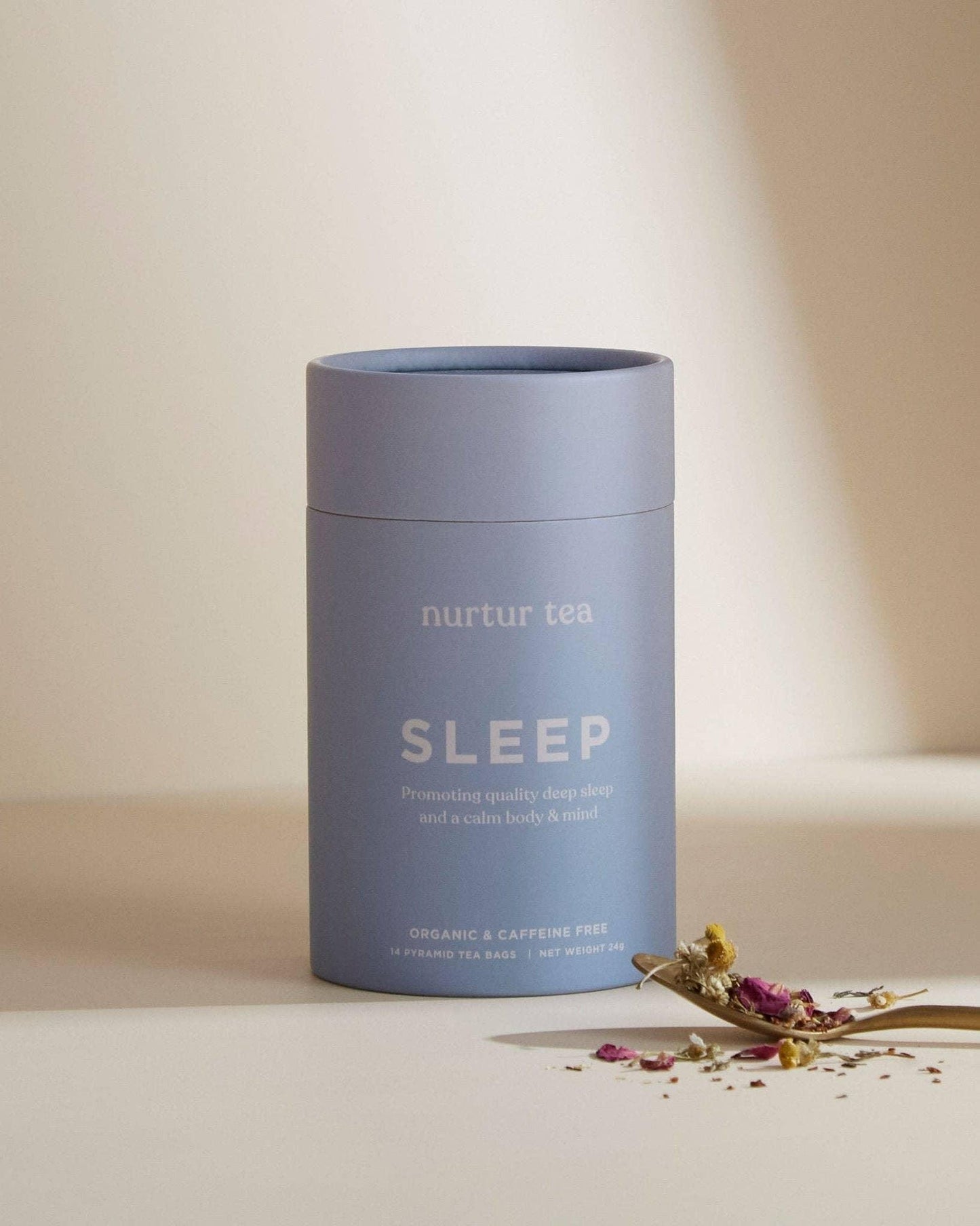 Blue container of nurtur tea sleep blend with dried flowers on spoon, promoting deep sleep. Come see us at Awaken, Franklin, Tennessee