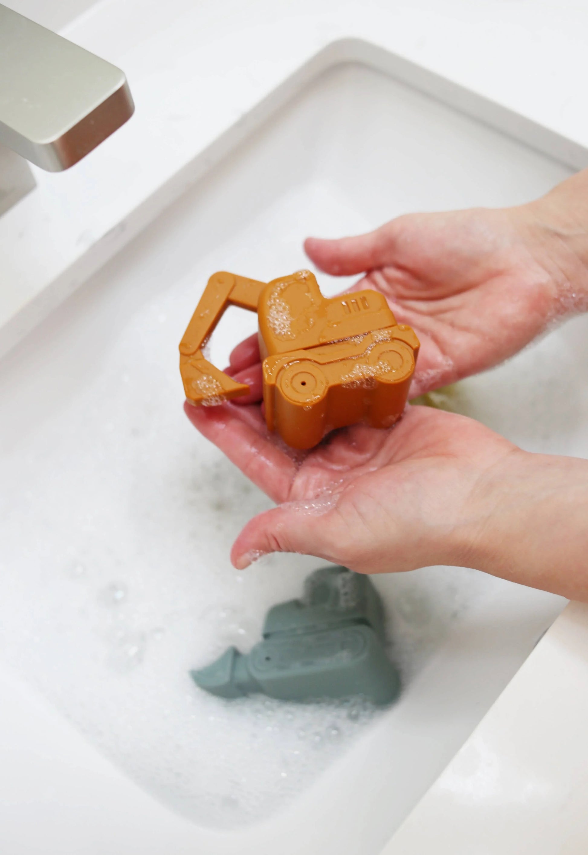 Hands washing a toy excavator in a white sink with foamy water, Come see us at Awaken, Franklin, Tennessee