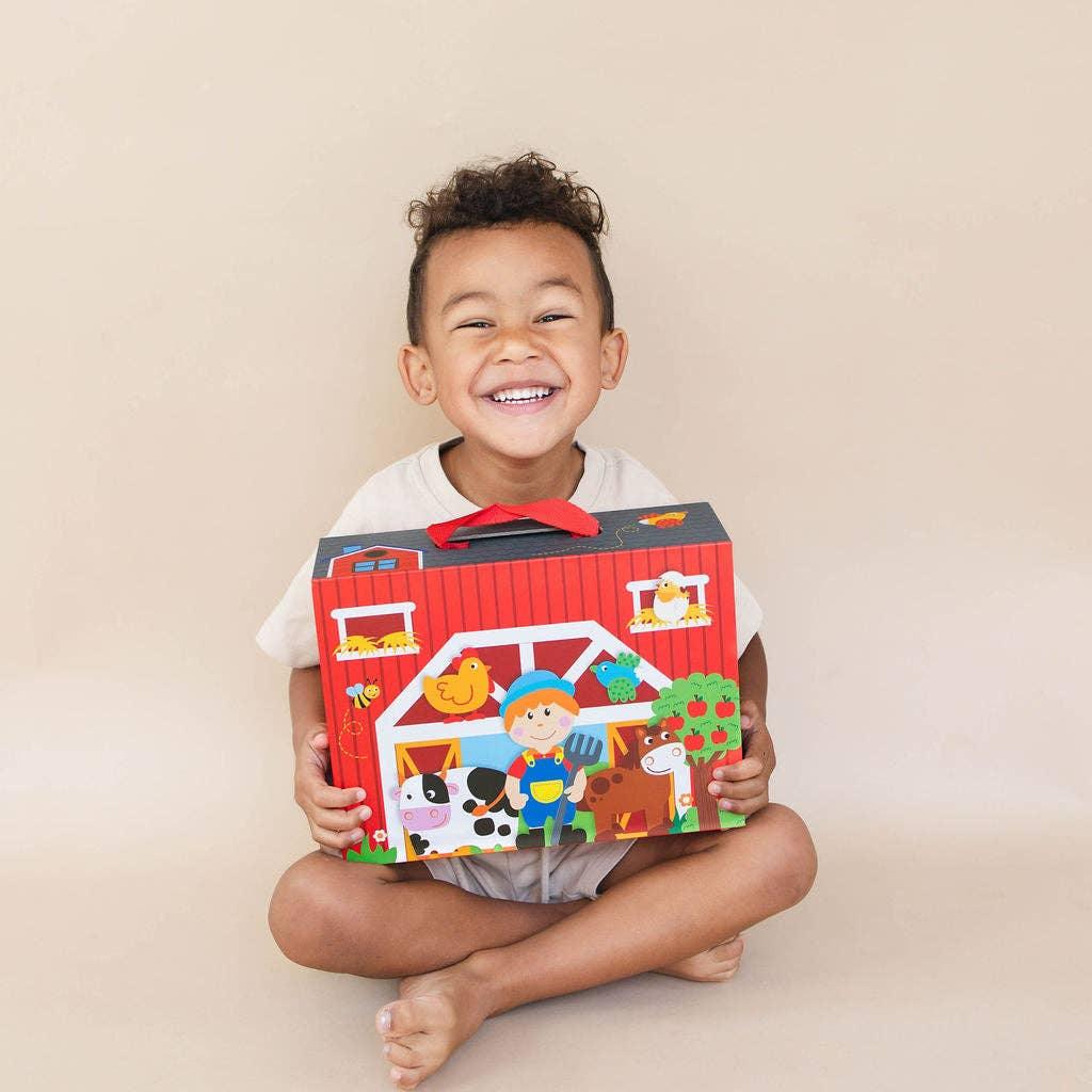 Smiling child sitting cross-legged holding colorful farm playset box, Come see us at Awaken, Franklin, Tennessee