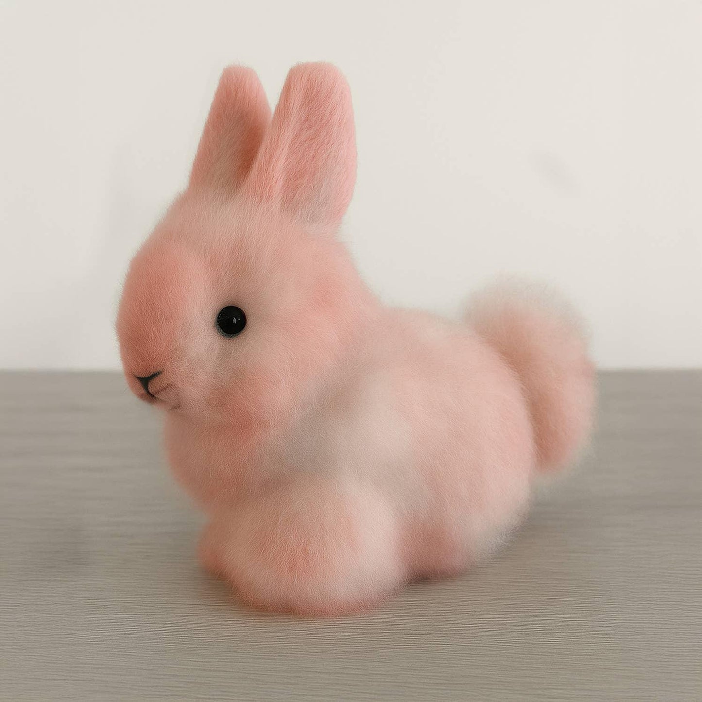 Soft pink plush bunny toy with black eyes on wooden surface. Come see us at Awaken, Franklin, Tennessee