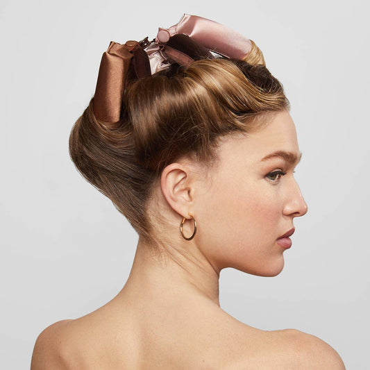 Side profile of woman with styled hair held by large brown and pink satin hair clips, wearing gold hoop earrings. Come see us at Awaken, Franklin, Tennessee
