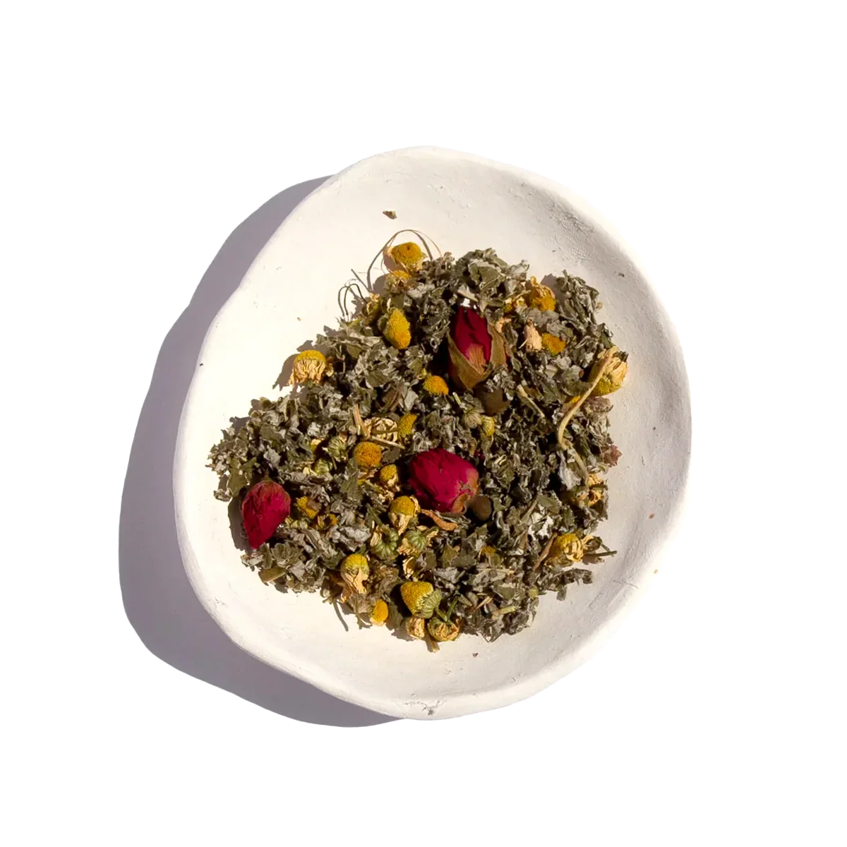 White ceramic bowl with dried herbal tea blend including chamomile and red rosebuds, bright background. Come see us at Awaken, Franklin, Tennessee
