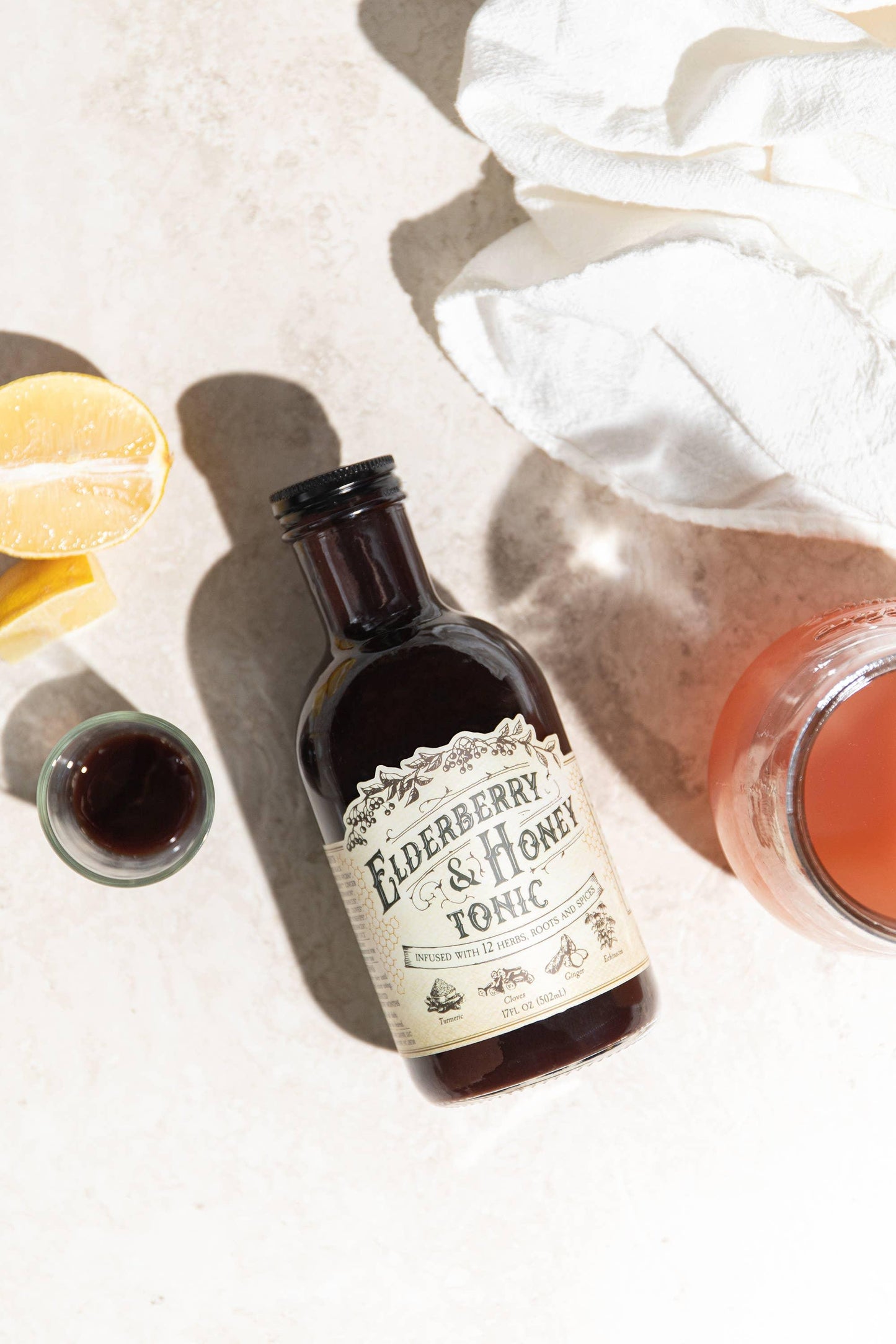 Elderberry & Honey Tonic bottle with lemon wedge and glass on light surface. Come see us at Awaken, Franklin, Tennessee
