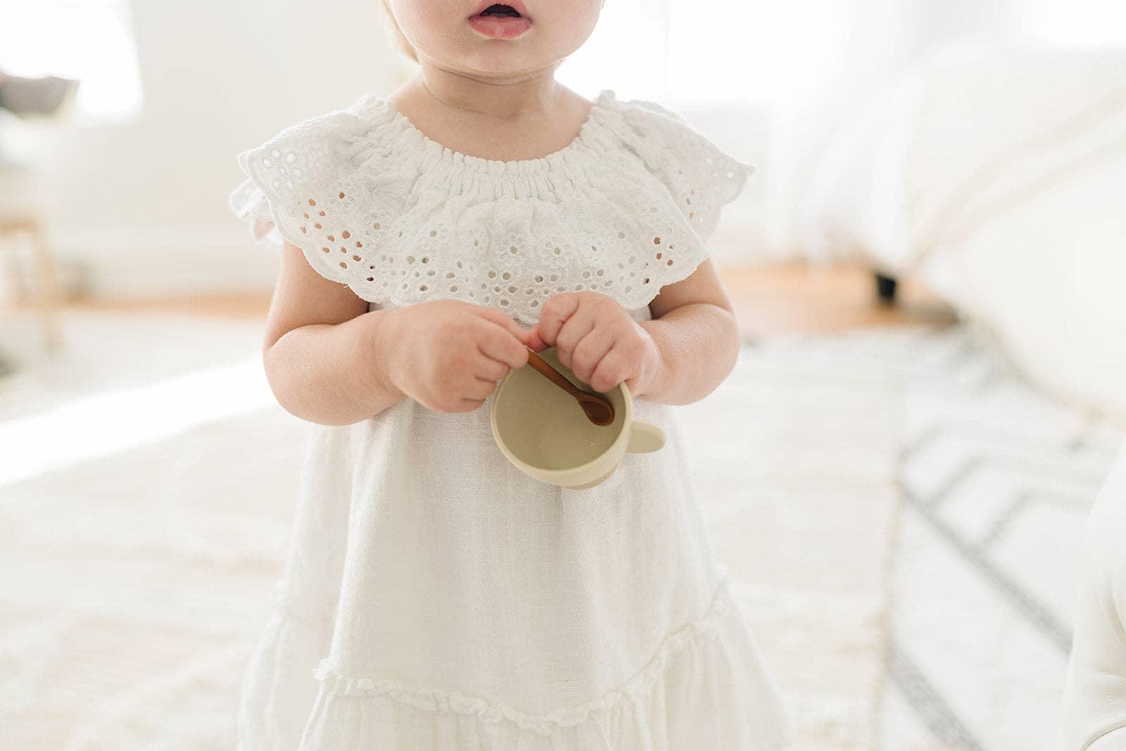 Toddler in white eyelet dress holding a cup, soft natural light, Come see us at Awaken, Franklin, Tennessee
