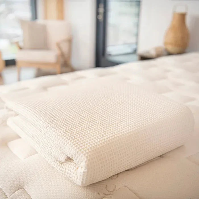 Folded waffle weave blanket on beige mattress in cozy bright bedroom Come see us at Awaken, Franklin, Tennessee