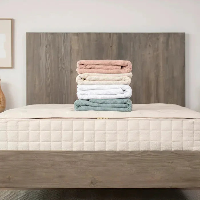 Stack of pastel waffle weave blankets on mattress with wooden headboard Come see us at Awaken, Franklin, Tennessee