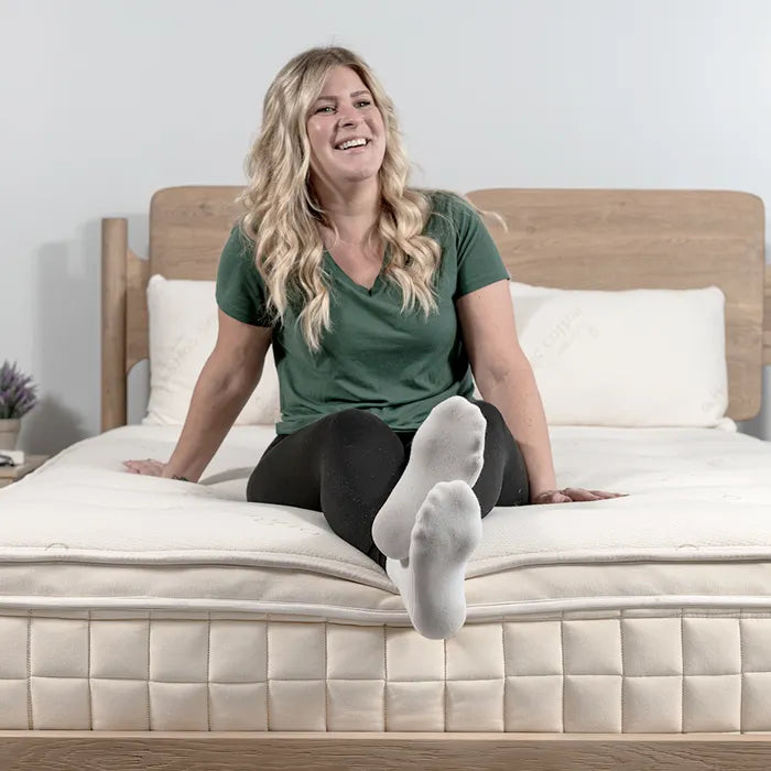 Smiling woman sitting on a mattress, wooden bed frame, Come see us at Awaken, Franklin, Tennessee