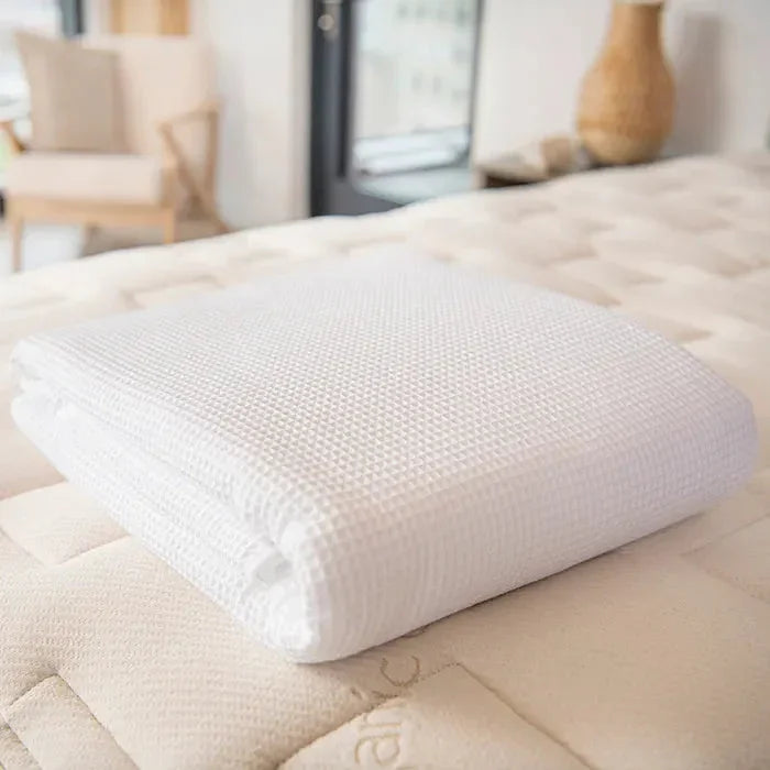 Folded white textured blanket on beige mattress in bright bedroom Come see us at Awaken, Franklin, Tennessee