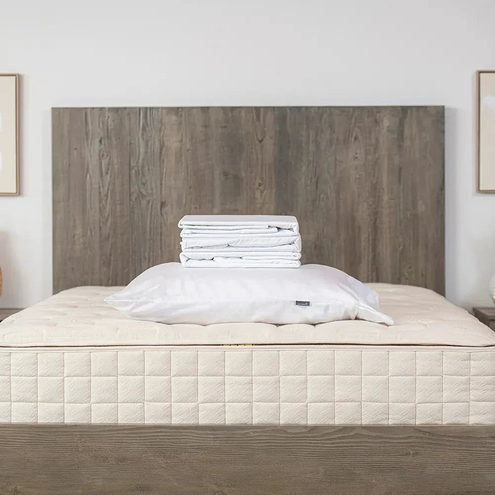 Stack of white bedding sheets and pillow on beige mattress with wood headboard. Come see us at Awaken, Franklin, Tennessee
